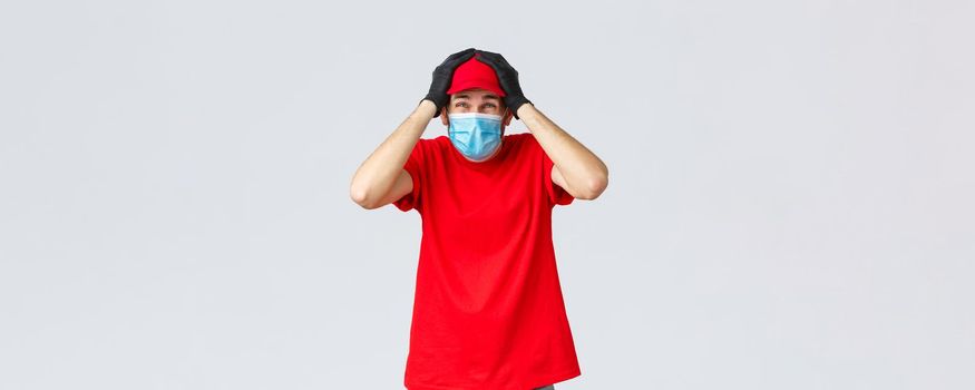 Covid-19, self-quarantine, online shopping and shipping concept. Troubled and anxious delivery guy cover head with hands, wear medical mask, gloves, something falling in storage, courier have trouble.