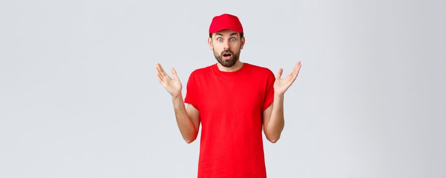 Online shopping, delivery during quarantine and takeaway concept. Confused and shocked courier in red t-shirt and cap of company service, raise hands up indecisive and nervous, cant believe smth.