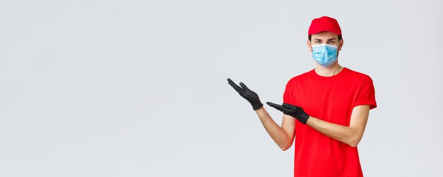 Groceries and packages delivery, covid-19, quarantine and shopping concept. Friendly delivery man in uniform, medical face mask and gloves introduce new promo, showing left banner.