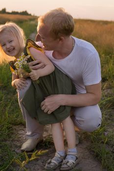 Dad and his blonde daughter are walking and having fun in a chamomile field. The concept of Father's Day, family and nature walks.