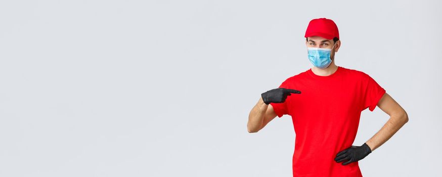 Covid-19, self-quarantine, online shopping concept. Confident smiling delivery guy in face mask, gloves in uniform, pointing himself. Courier provide fast shipping during coronavirus outbreak.