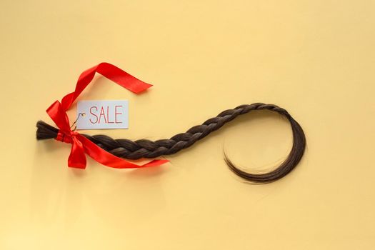 Long brown braid with tag label and red ribbon on yellow background, haircut sale service, material of natural hair for model hairstylish extension, top view