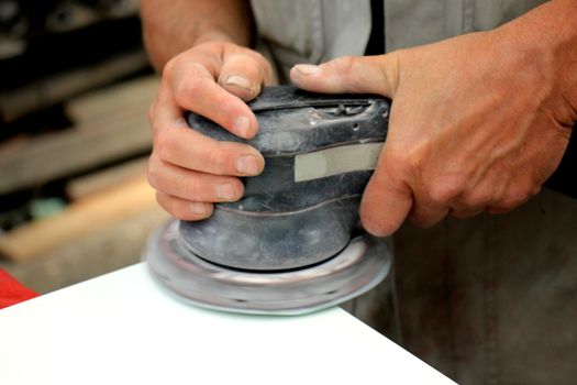 Man in vehicle repair shop, sanding a car part with a grinding machine