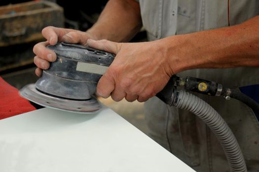 Man in vehicle repair shop, sanding a car part with a grinding machine