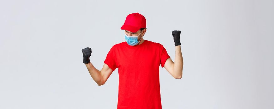 Covid-19, self-quarantine, online shopping and shipping concept. Encouraged and confident delivery man fist pump, feel empowered and happy, fist pump yell yes, accomplish goal, wear face mask.