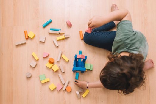 top view of a child little girl playing on the floor with wooden building block toys at home or kindergarten, educational toys for creative children