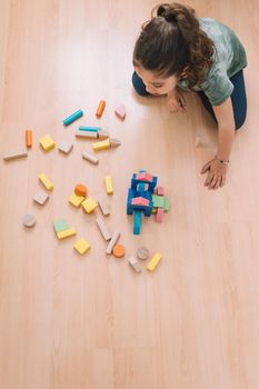 top view of a child little girl playing on the floor with wooden building block toys at home or kindergarten, educational toys for creative children, vertical photo