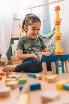 smiling little girl playing happy in the floor with colorful wooden building block toys at home or kindergarten, educational toys for creative children
