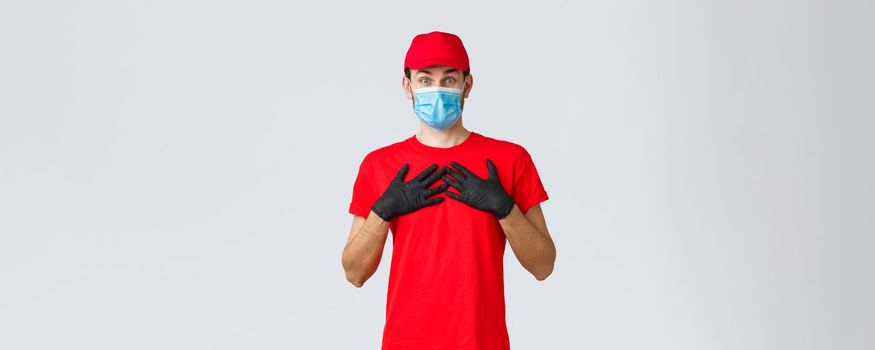 Covid-19, self-quarantine, online shopping and shipping concept. Is it for me, touched and surprised delivery guy receive gift or compliment, press hands chest flattered, wear face mask and gloves.
