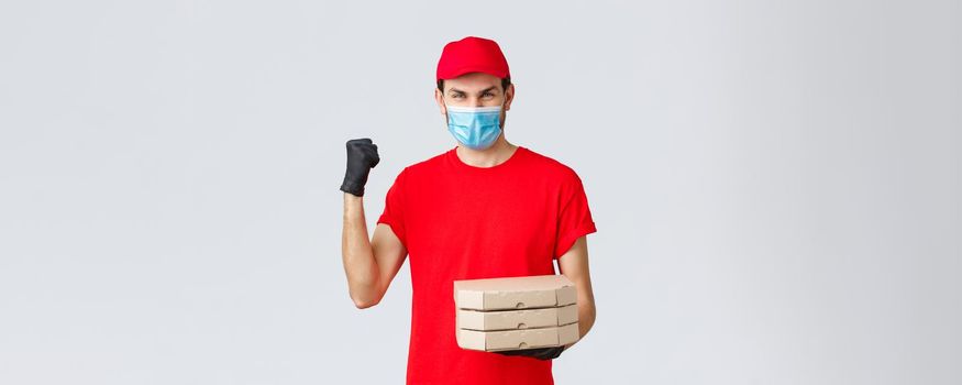 Food delivery, application, online grocery, contactless shopping and covid-19 concept. Fast and safe delivery, champions in industry. Courier in red uniform fist pump, deliver pizza order.