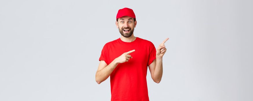 Online shopping, delivery during quarantine and takeaway concept. Enthusiastic smiling courier in red uniform cap and t-shirt, pointing fingers right, showing banner, recommend special offer.