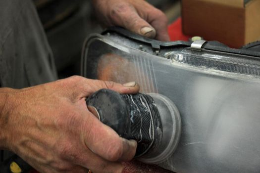 Man polishing a car headlight with sanding machine and fine sandpaper