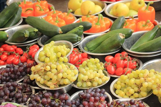 Fresh fruits and vegetables on a market stall: grapes, tomatoes, courgette and peppers displayed in small metal bowls