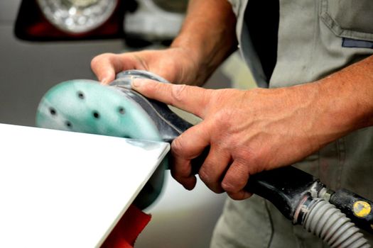 Man in vehicle repair shop, sanding a car part with a grinding machine