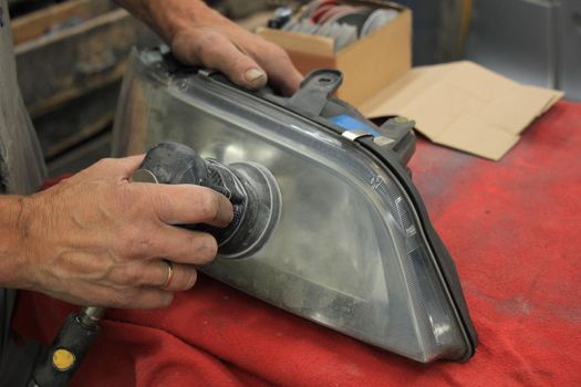 Man polishing a car headlight with sanding machine and fine sandpaper