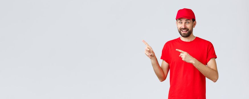 Online shopping, delivery during quarantine and takeaway concept. Amused and excited smiling courier inviting client take look, employee in red uniform cap and t-shirt pointing fingers left.