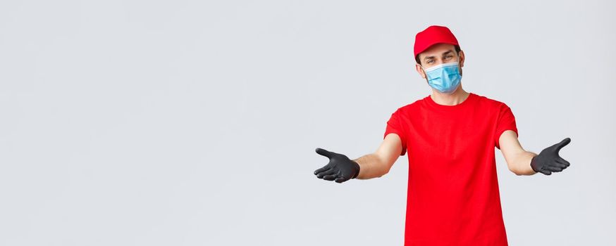Covid-19, self-quarantine, online shopping and shipping concept. Friendly delivery man in face mask and gloves, reaching hands to receive package from client, provide delivering during coronavirus.