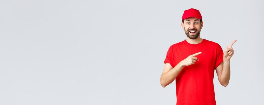 Online shopping, delivery during quarantine and takeaway concept. Enthusiastic smiling courier in red uniform cap and t-shirt, pointing fingers right, showing banner, recommend special offer.