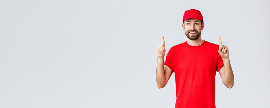 Online shopping, delivery during quarantine and takeaway concept. Smiling cheerful courier in red t-shirt, cap pointing fingers up. Employee look intrigued at banner with special discount.