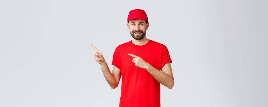 Online shopping, delivery during quarantine and takeaway concept. Friendly handsome bearded employee, courier in red uniform cap and t-shirt, pointing fingers left, inviting client take look.