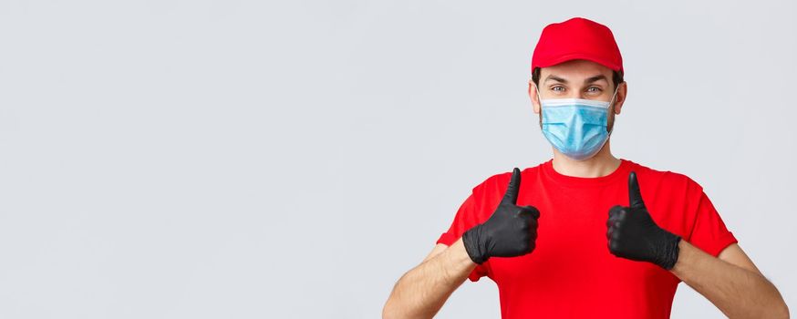 Contactless delivering, covid-19 and shopping concept. Cheerful courier or employee in face medical mask and gloves, show thumbs-up in approval, recommend using order shipping service.