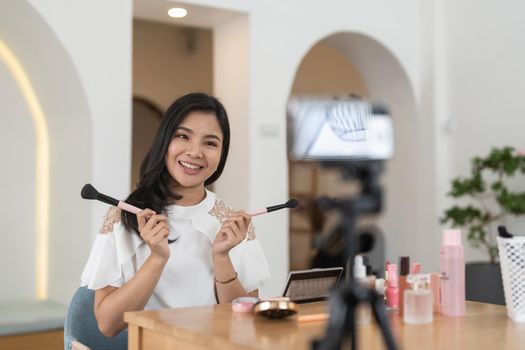 Asian female beauty blogger live streaming to review makeup product on social media, Modern young woman influencer demonstrating her daily cosmetic while talking on smartphone camera.