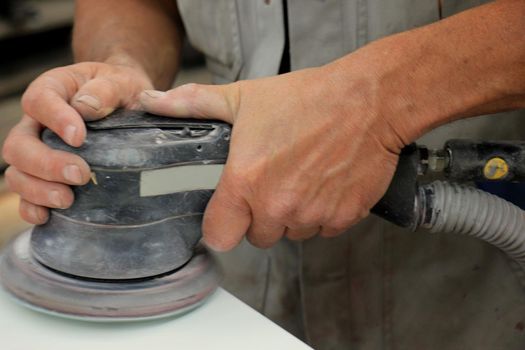 Man in vehicle repair shop, sanding a car part with a grinding machine