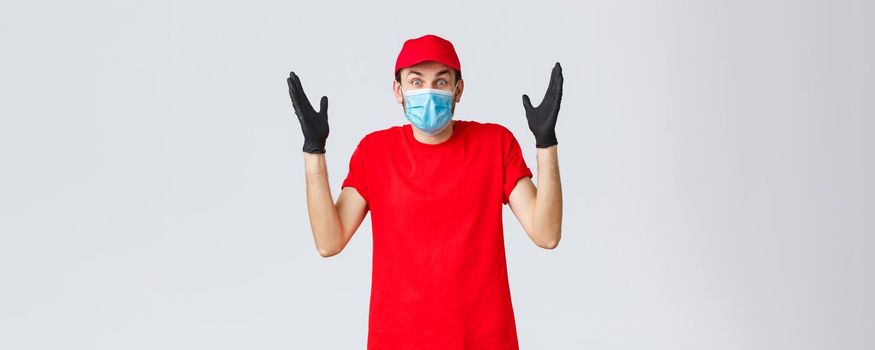 Covid-19, self-quarantine, online shopping and shipping concept. Surprised and confused delivery guy in medical mask, gloves and re duniform, shrugging, cant understand how it happened.