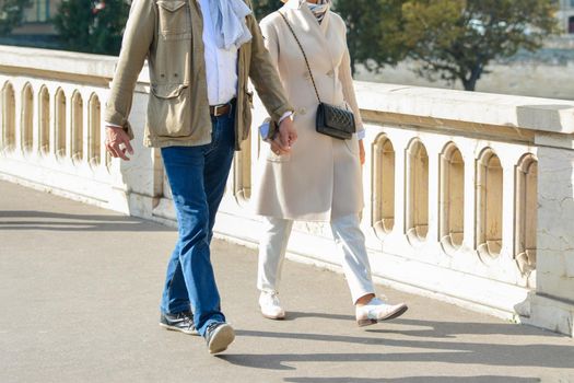 An elderly well dressed couple is walking and holding hands in a Paris
