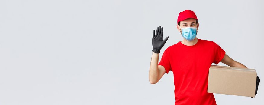 Packages and parcels delivery, covid-19 quarantine delivery, transfer orders. Friendly courier in red uniform, face mask with protective gloves, deliver order box to client, waving hand in hello.