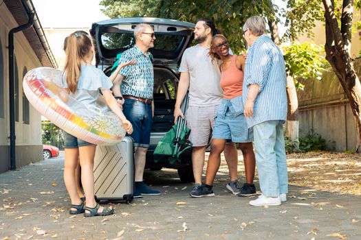 Diverse family and friends travelling on vacation at seaside, going by car with luggage and suitcase. Child, parents and grandparents leaving on summer holiday trip with baggage and inflatable.