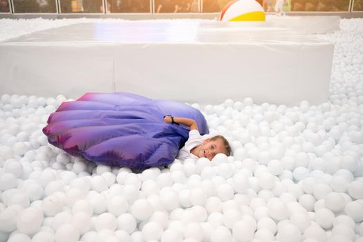 Happy little girl playing white plastic balls pool in amusement park. playground for kids. Active leisure for children.