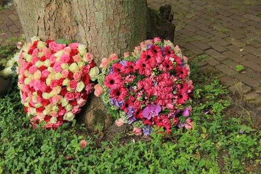 Heart shaped sympathy flowers near a tree at a cemetery