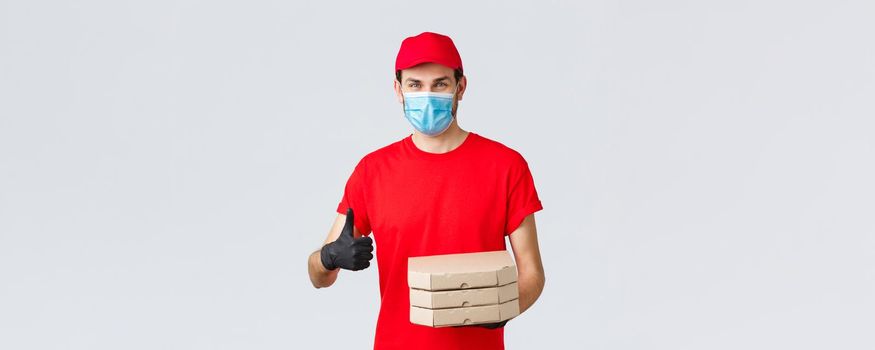 Food delivery, application, online grocery, contactless shopping and covid-19 concept. Smiling caucasian courier in red uniform, gloves and face mask, provide best offers, pizza express delivery.
