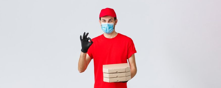 Food delivery, application, online grocery, contactless shopping and covid-19 concept. Courier guarantee quality of pizza, holding boxes, showing okay sign in recommendation or approval, wear mask.