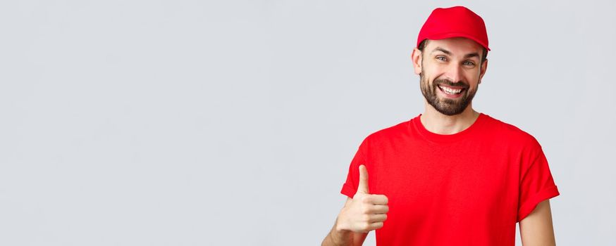 Online shopping, delivery during quarantine and takeaway concept. Friendly, cheerful courier in red cap and t-shirt uniform, encourage make internet orders, thumb-up in approval or recommendation.