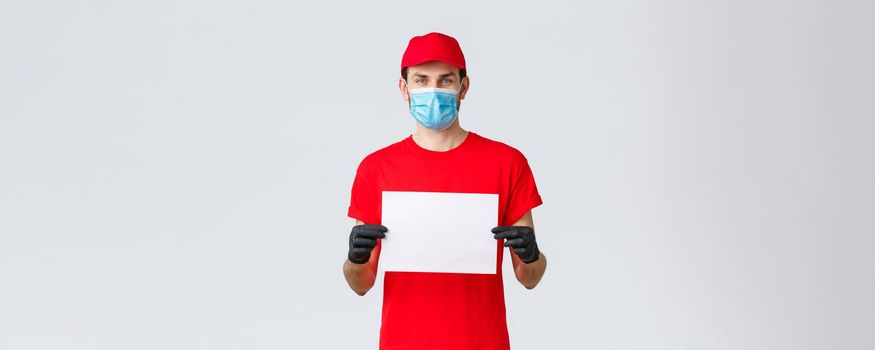 Covid-19, self-quarantine, online shopping and shipping concept. Express delivery guy during coronavirus tell stay safe home, buy internet, holding blank piece paper for your info, wear face mask.