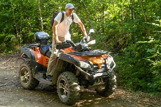 Young man driving off road adventure with happy and smiling. Man riding on ATV bike or quad bike on road along forest trail on mountain. Camping, jungle adventure concept