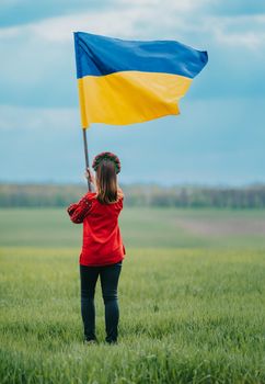 Beautiful ukrainian woman with national flag on green field background. Young lady in red embroidery vyshyvanka. Ukraine, independence, freedom, patriot symbol, victory in war. High quality photo