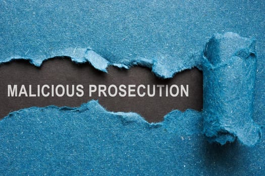Words malicious prosecution on paper under blue one.