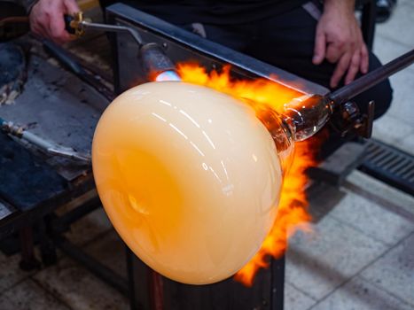 Glass artist forms the scorching glass with heats it with a gas burner torch. Closeup of the artist's method. Czech hand made glass studio.