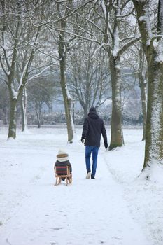 Father and son walking in the snow with a small sleigh