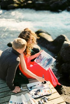 Man looks over the shoulder of a woman painting a picture. High quality photo