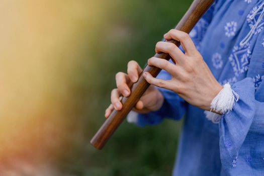 Woman playing woodwind wooden flute - ukrainian sopilka outdoors. Folk music, culture concept. Musical instrument. Lady in traditional embroidered shirt - blue vyshyvanka. High quality photo