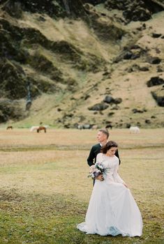 Bride with a bouquet stands next to her groom in a mountain valley. Iceland. High quality photo