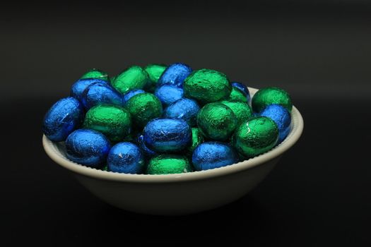 Foil wrapped chocolate easter eggs in a white porcelain bowl