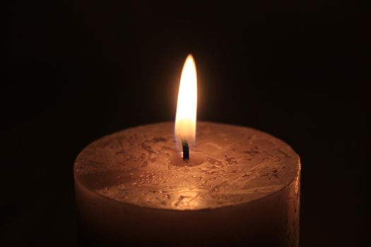 Closeup of a big burning candle , dark color