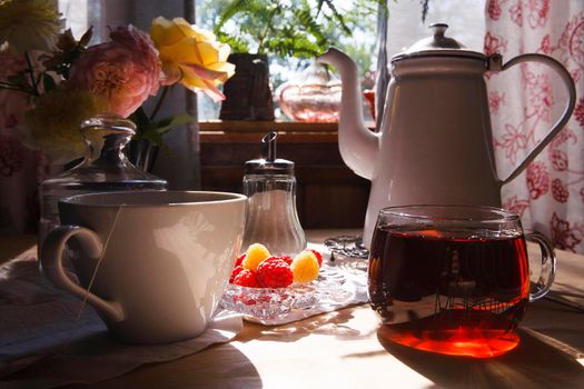 White teapot and two cup with tea, bouquet of yellow roses and raspberry on white table in vintage country kitchen, summer morning concept, selective focus