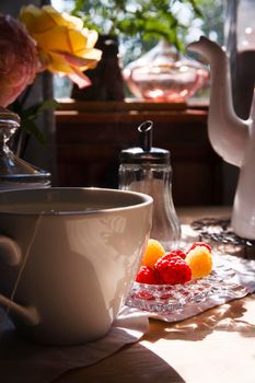 White cup of tea and raspberry on plate on white table in vintage country kitchen, summer morning concept, selective focus