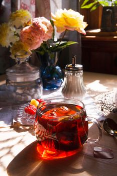 A cup of tea and bouquet of yellow roses and raspberry on white table in rustic kitchen, summer morning concept, selective focus, bright light with shadows.